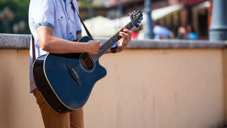 young guy playing an acoustic guitar on a city streetの写真素材