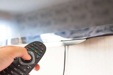 remote control in hand pointing at TV