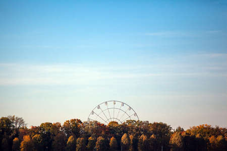 ferris wheel over trees against a blue skyのeditorial素材