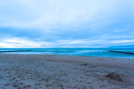 wide sandy beach with a breakwater by the cold sea in cloudy weather on long exposureの写真素材