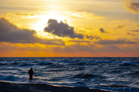 silhouette of a man in a diving suit with a net on the beach collecting amber in the water against...