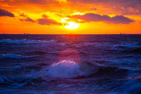 rich bright orange sun in a cloudy sky over the sea during sunsetの写真素材