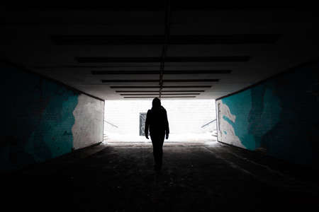 silhouette of a lonely man in a dark tunnel on a bright backgroundの写真素材