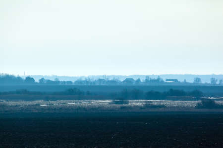 minimalistic beautiful landscape in blue colors with the silhouette of a small village in the morning mist and forest in the backgroundの写真素材