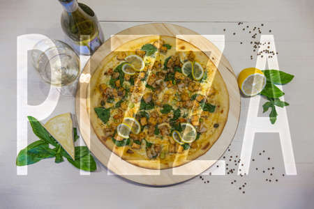 appetizing pizza with shrimps, lemon and a glass of wine on a white table with the inscription "PIZZA", flat layの写真素材