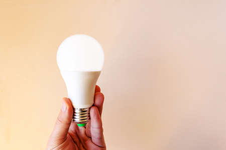 modern bright LED light bulb in hand on a beige background, copy spaceの写真素材