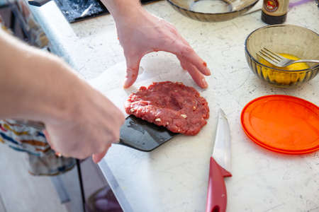 young guy in the brightly lit kitchen preparing meat patties