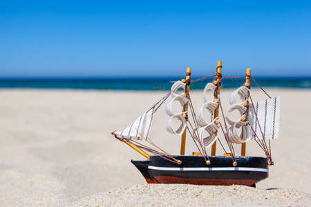 small toy ship on a sandy beach on the background of the sea, concept