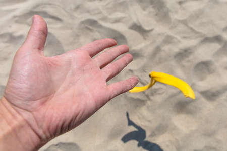 hand throwing banana peel on the beach