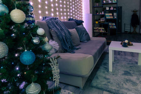 interior of a dark cozy room with a sofa, Christmas tree and garlands on the wallの写真素材