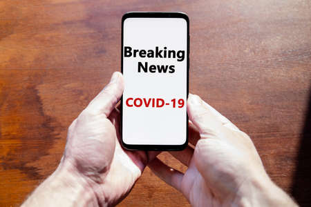 smartphone in hand with the inscription "breaking news covid-19" on the displayの写真素材