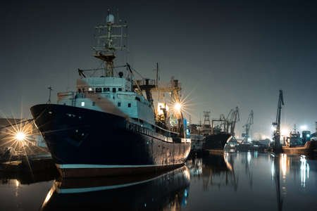 large fishing boat in the night port with cranes in the background