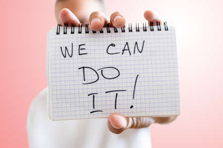 sheet of paper with the inscription WE CAN DO IT in hand on light red backgroundの写真素材