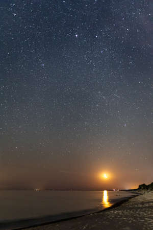 night starry sky with rising moon over sea beachの写真素材