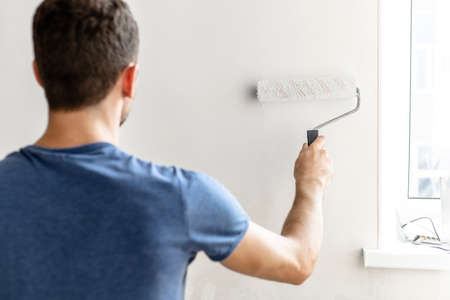 a man paints the wall with a roller white