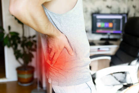 a man holds his back in pain against the background of the roomの写真素材