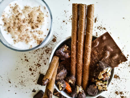 Chocolate bars, chocolates, chocolate tubes sprinkled with cocoa in a white bowl with a glass of milk next.の写真素材
