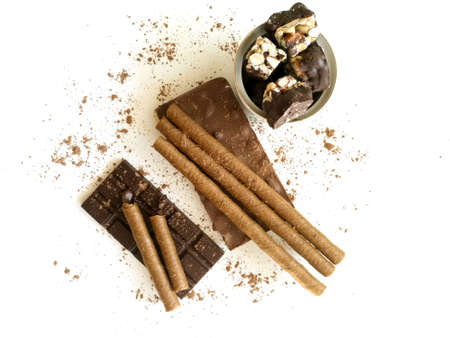 Various types of chocolate, chocolate tubes on a white table, sprinkled with cocoa powder, coffee beansの写真素材