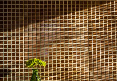 a small green vase with flowers on the background of a square kitchen tile in the light of sunlight at sunriseの写真素材