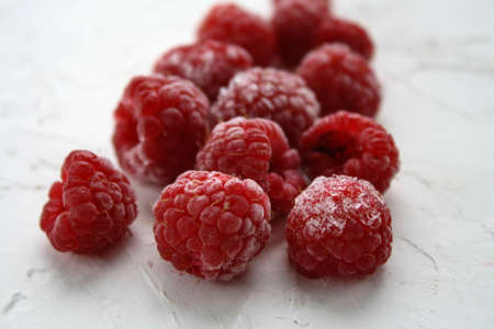 Ripe, frozen raspberries lie on a white surface covered with frostの写真素材