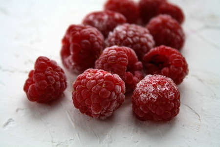 Ripe, frozen raspberries lie on a white surface covered with frostの写真素材