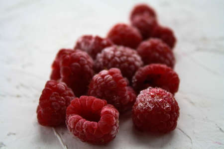 Ripe, frozen raspberries lie on a white surface covered with frostの写真素材