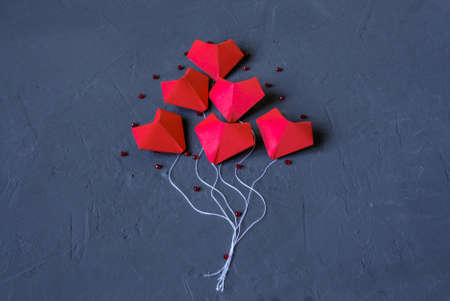 Origami red hearts made of paper on a dark blue background laid out in the form of balloons flying into the air. Valentine day. Free space for design.の写真素材