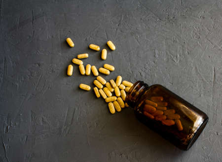 Yellow pills scattered on a black surface near a glass overturnedの写真素材