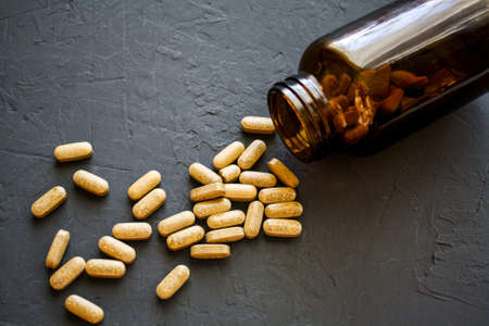 Yellow pills scattered on a black surface near a glass overturned vial. Medications for the virus, supplements for pregnant womenの写真素材