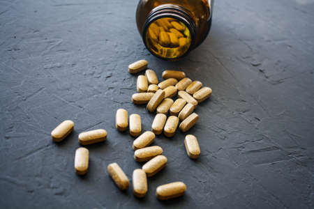 Yellow pills scattered on a black surface near a glass overturned vial. Medications for the virus,...