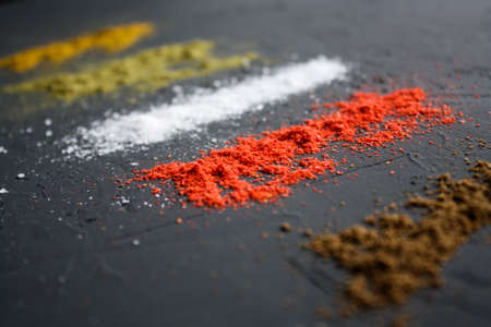 Vertical paths of different spices located on a black surface.の写真素材