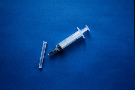 A syringe without a package filled with yellow medicine located on a blue background in the center of the composition.の写真素材