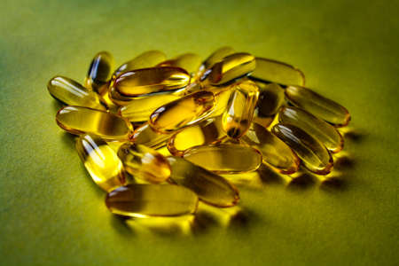 Fish oil capsules are scattered on the yellow surface.の写真素材