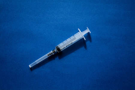 A syringe without a package filled with yellow medicine located on a blue background in the center of the composition.の写真素材