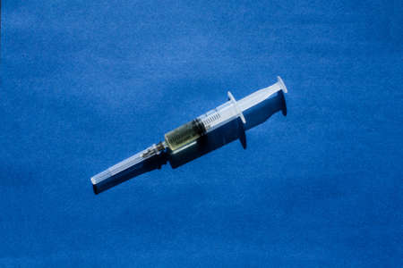 A syringe without a package filled with yellow medicine located on a blue background in the center of the composition.の写真素材