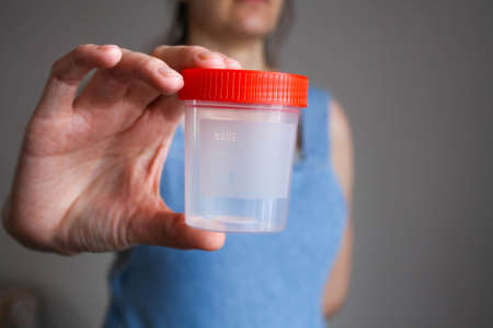A young pregnant woman holds a test container in front of her.の写真素材
