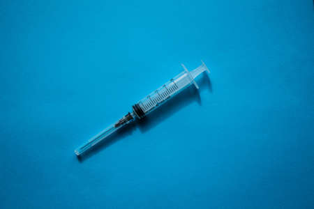 A syringe without a package filled with yellow medicine located on a blue background in the center of the composition.の写真素材