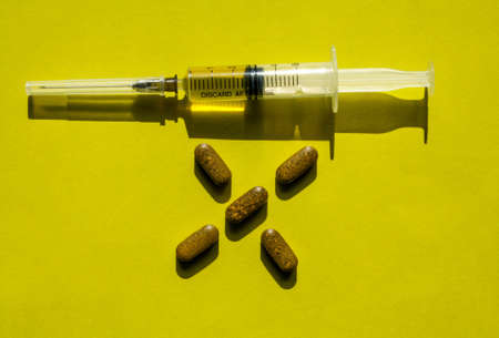 A syringe ready for use and a handful of tablets, on a yellow surface.の写真素材