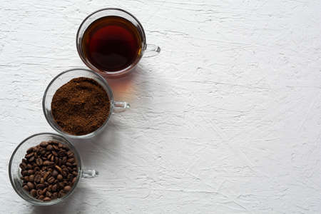 Three clear glass cups with ground coffee, coffee beans and brewed coffee in one row on a white backgroundの写真素材