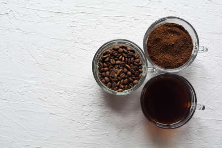 Three clear glass cups with ground coffee, coffee beans and brewed coffee in one row on a white backgroundの写真素材