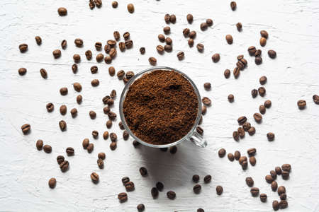 A Cup filled with coffee beans. Coffee beans are scattered on the white surface of the tableの写真素材