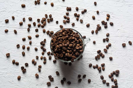 A Cup filled with coffee beans. Coffee beans are scattered on the white surface of the tableの写真素材
