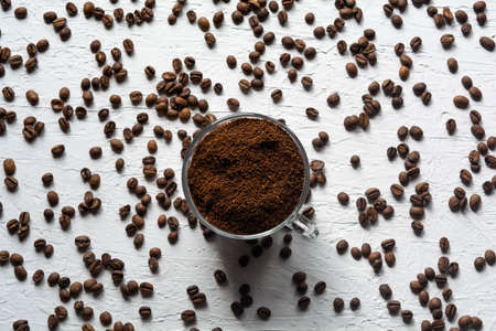A Cup filled with coffee beans. Coffee beans are scattered on the white surface of the tableの写真素材