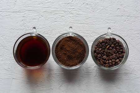 Three cups of ground coffee, coffee beans and brewed coffee in one rowの写真素材
