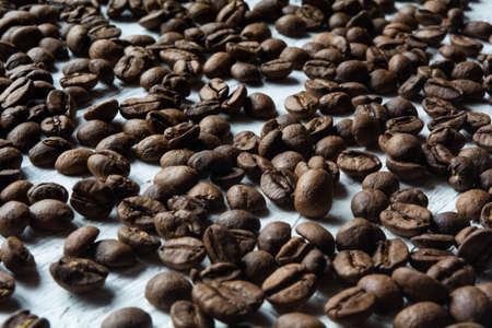 Roasted coffee beans scattered on a white surfaceの写真素材