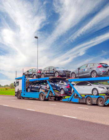 Truck trailer carrying several cars on a highway on a cloudy dayの写真素材