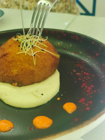 Fried croquette with mashed potatoes on a black plate.