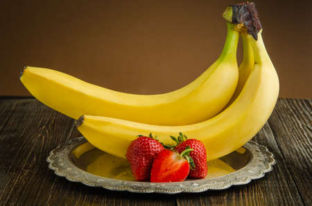 Bananas with strawberries on a vintage plate.の写真素材