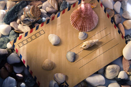 Yellow envelope, shells in a glass jar on pebble background with warm light. . Top view.の写真素材
