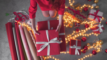 Girl creates New Years packages with red paper, colored ribbons. A young woman is packing Christmasの写真素材